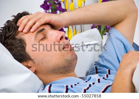 Close up of young man lying down in bed taking temperature and having flu