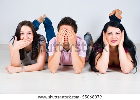 Three cheerful friends lying down on wooden floor and gesturing speak,see and hear no evil