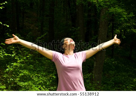 Young woman standing with arms open  and eyes closed to breath the clean air  from a spring forest