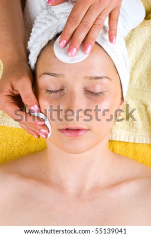Beautician cleansing young woman face with pure cotton cosmetic pads and lotion in a spa resort