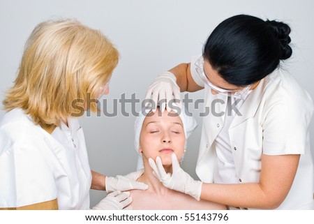 Two doctors examine woman face skin and preparing her for a procedure