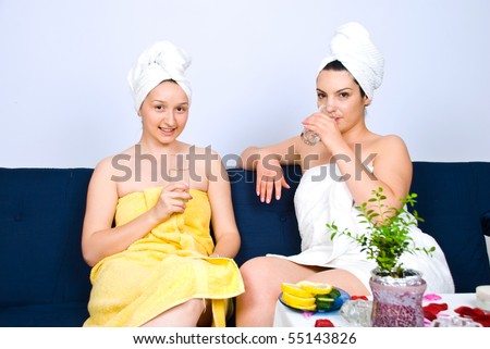 Two beautiful women friends  sitting together on couch in a waiting room at  spa center,they drinking water and smiling for you