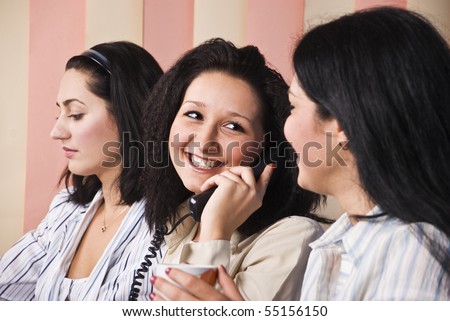 Three business women in office,the middle woman speaks by phone and laughing with her colleague