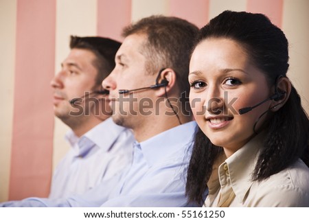 People with headset working in a call center,young woman facing and smiling at you and men standing in profile