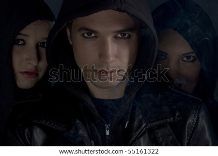 Bad boys concept,street people in darkness .Young man  the head of the  band  in front of two woman  with smoke around them