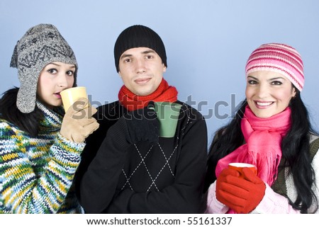 Friends in warm clothes with caps,pullovers and gloves enjoying a hot drink together and  smiling over blue background