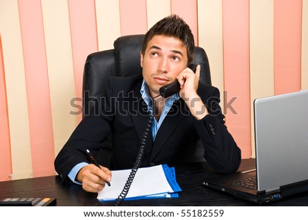 Thoughtful business man talking at phone and writing on papers at desk in office