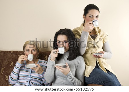 Three women friends enjoying a coffee and a conversation in living room,sitting all on sofa