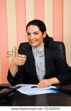 Elegant business woman sitting on chair at desktop in her office and giving thumbs up