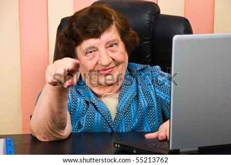 Elderly  business woman sitting on chair at desk in office and pointing to you:Yes,you!