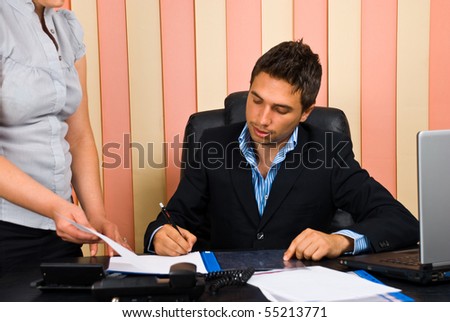 Boss sitting on chair in office signing  his secretary documents
