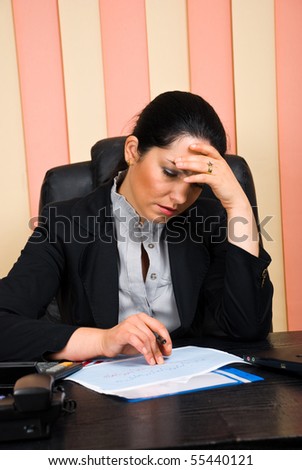 Sad  financial consultant woman with problems  looking over some  sales graphs and holding hand on forehead