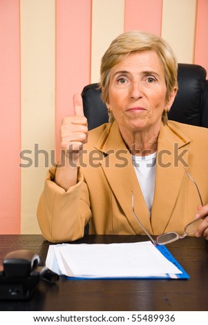 Aged woman sitting at desk in office give thumb up