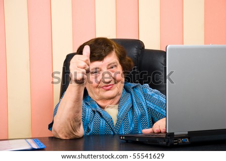 Older corporate woman giving  thumbs up and sitting at desktop