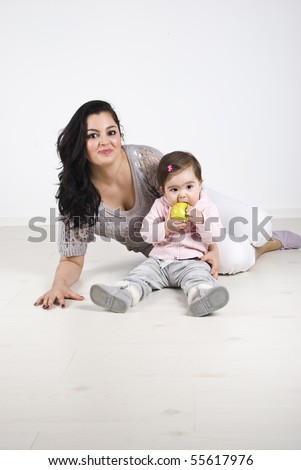 Happy mother and her little girl sitting on wooden floor and the baby holding and eating a green apple