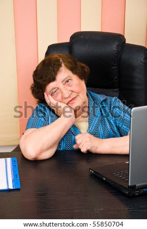 Sad elderly business woman sitting  on chair at desk in office and holding hand to face