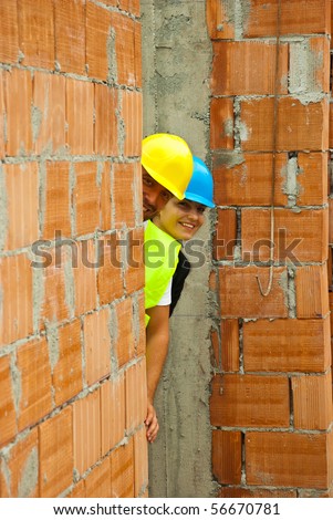 Two young architects hidden behind wall laughing and having fun at work