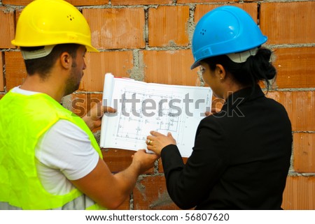 Back of two architects with helmet working in a house under construction and holding blueprints,selective focus on plan