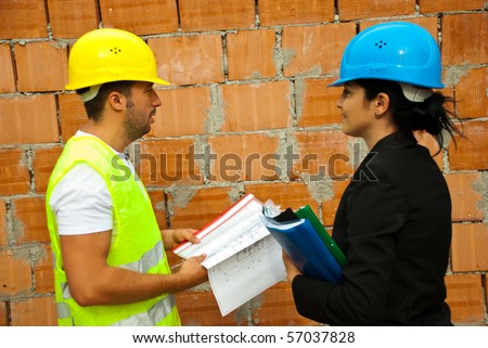 Two architects holding projects and  folders standing in profile and having a conversation on site