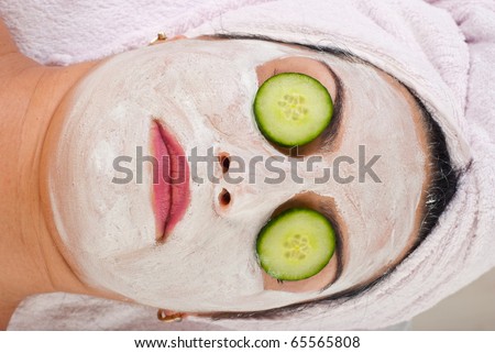 Detail of horizontally head shot of woman with facial mask and slices cucumber on eyes