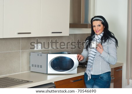 Attractive woman drinking coffee and opening microwave oven in her kitchen