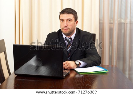 Serious manager with laptop and folders sitting on chair in a meeting room