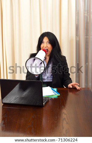 Crazy manager woman sitting on chair at table and shouting in megaphone
