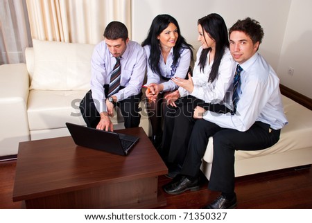 Four business people having a discussion,using laptop and sitting all  on a beige couch in a workplace