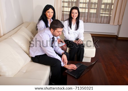 Three business people team sitting on sofa in a workplace and business man using a laptop