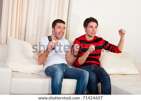 Two excited men sitting on couch and watching favorite team soccer with goal