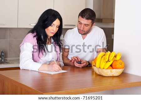 Serious mid adult couple standing in their kitchen and writing and calculate their expenses