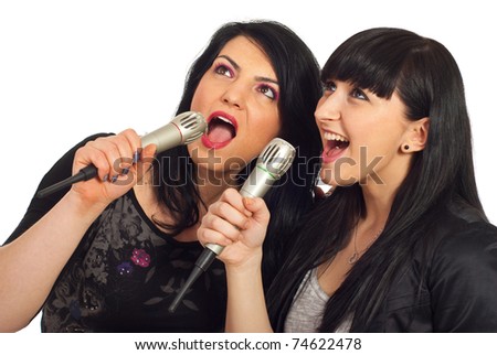 Happy beauty two women singing in microphones at karaoke party and looking up to screen isolated on white background