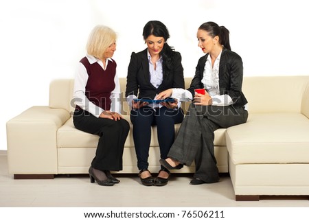 Three business people having conversation ,looking over folders  and sitting on a beige sofa in office