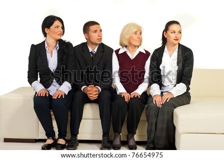 Four business people sitting in a row on sofa and looking in right part of image with different facial expressions on their faces