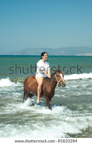 Laughing woman riding horse in water sea with waves