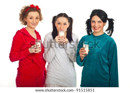 Happy three friends women in pajamas standing in a line and holding milk glasses isolated on white background