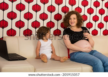Pregnant mom drinking water and having conversation with her toddler son on sofa home