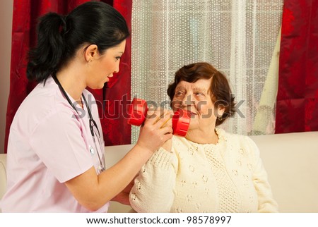 Therapist helping elderly woman to making exercisies with dumbbell home