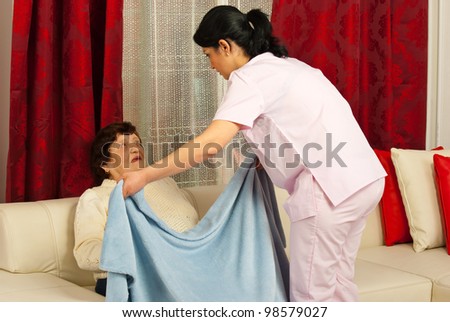 Nurse woman covering elderly woman with a blanket in her home