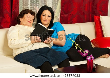 Grandma reading from a book to her adult granddaughter in living room