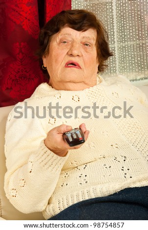 Elderly woman holding remote control and watching tv home