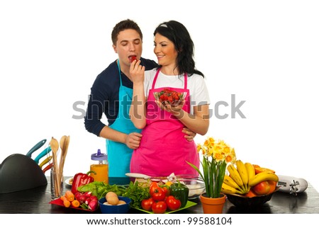 Happy woman giving to her husband to eat strawberry in their kitchen against white background