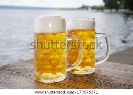 Two Beer Mugs with fresh Beer and Foam in a Beer Garden at Lake, close up / Fresh Beer
