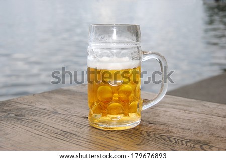 Beer Mug with fresh Beer and Foam in a Beer Garden at Lake, close up / Fresh Beer