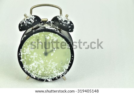 close up of  a snowy, frozen,  black retro alarm clock,  showing winter time, 2 am, horizontal  / Clock Change Winter Time