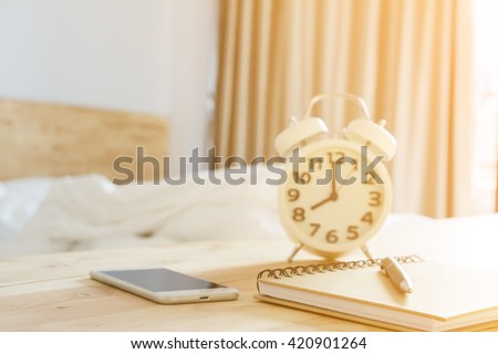 pen on notebook, smartphone alarmclock in bed room with lighting morning time selective focus and blurred background