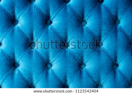 Coach-type velours screed tightened with buttons. Blue chesterfield style quilted upholstery backdrop close up. Capitone pattern texture background