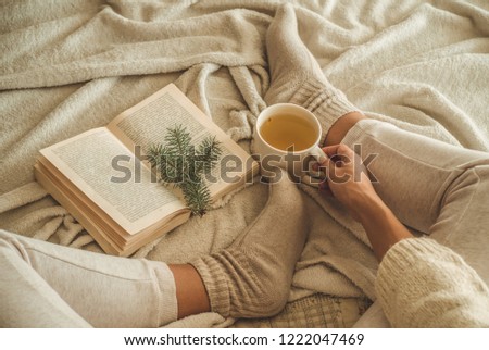 Cozy winter evening , warm woolen socks. Woman is lying feet up on white shaggy blanket and reading book. Cozy leisure scene. Text in book is unreadable. Woman relaxing at home. Comfy lifestyle.