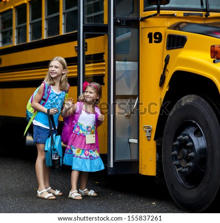 Two grade school girls getting on school bus for first day of school.