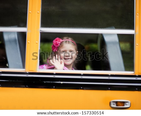Young girl waving from school bus window